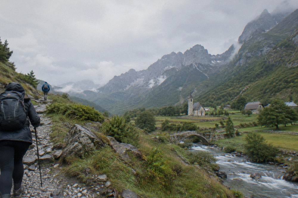 Hikers on a stony mountain trail crossing a pass between two green valleys