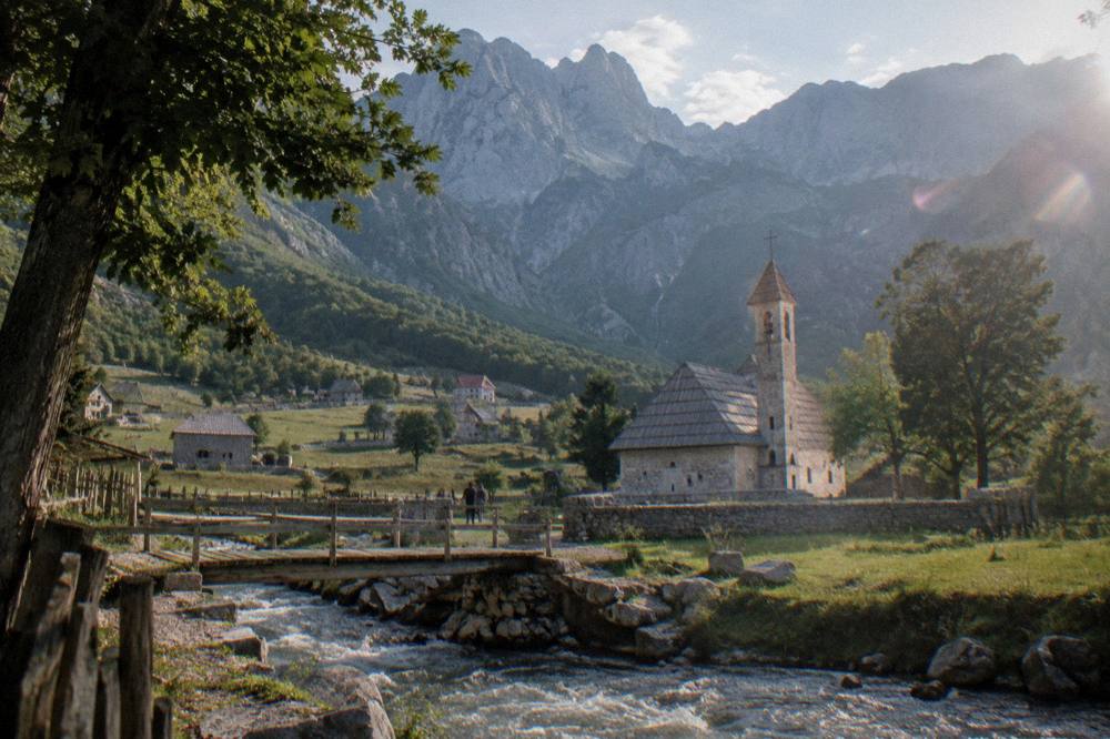 A small stone church with a wooden shingle roof standing in a high mountain valley
