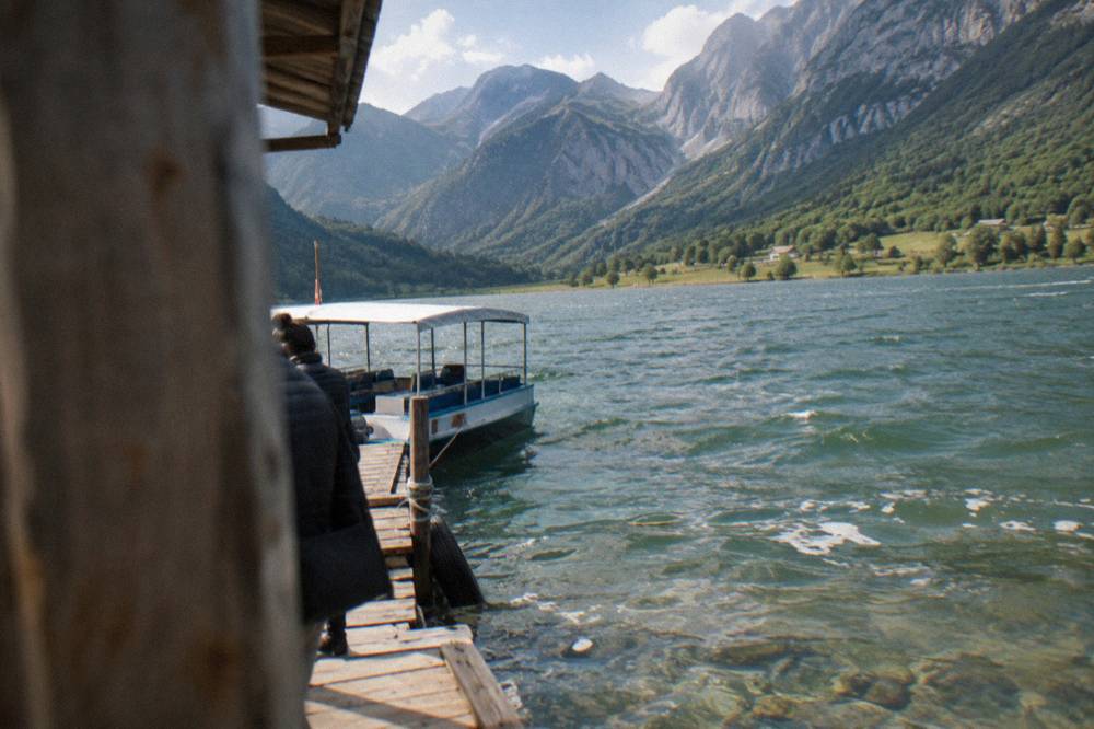 Small passenger boat moored at a wooden jetty on a green mountain lake