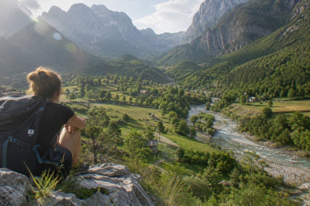 Hiker with a backpack resting on a rock above a wide green valley
