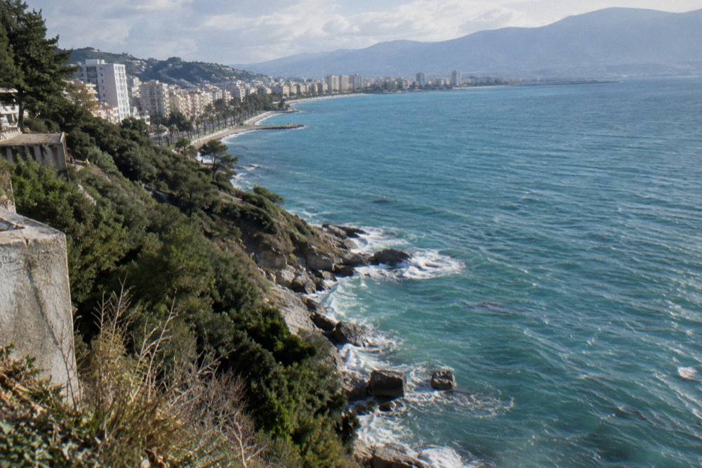 Turquoise water breaking on smooth rocks below steep green hillsides