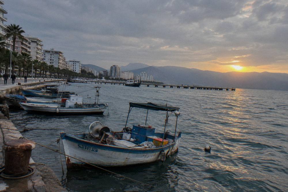 A calm bay at sunset with moored fishing boats and a long pier