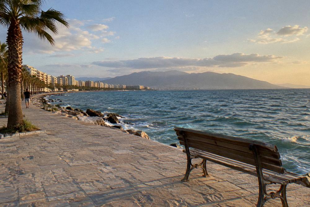 A stone promenade at golden hour with an empty bench facing the open sea