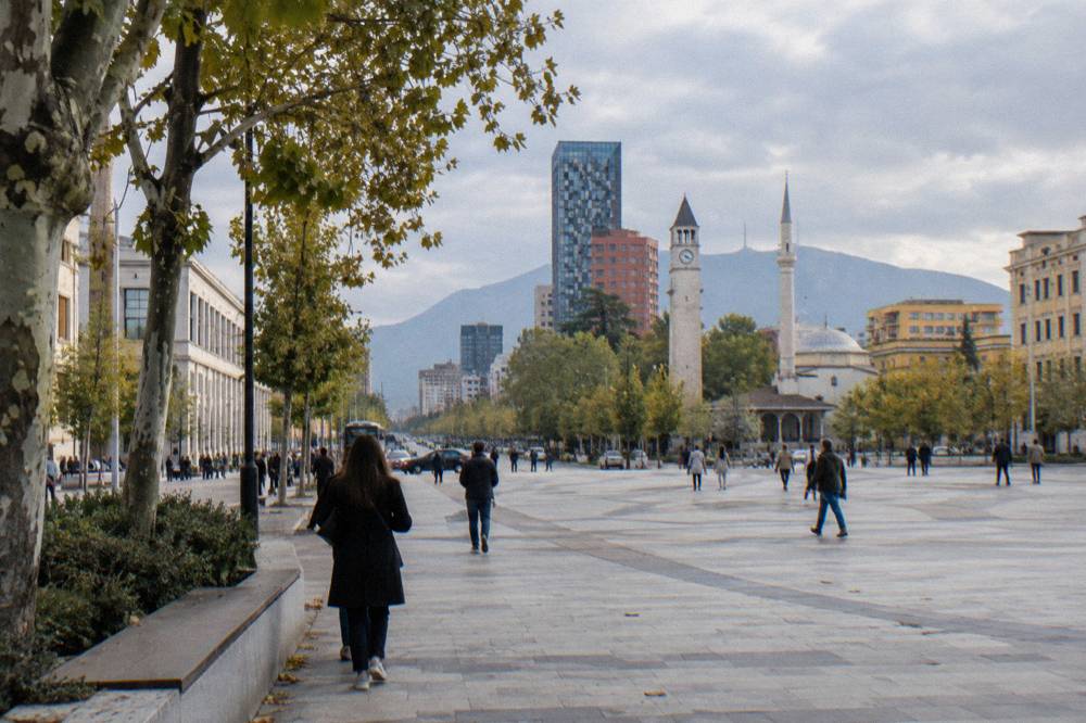 A wide city boulevard in Tirana with modern buildings and trees