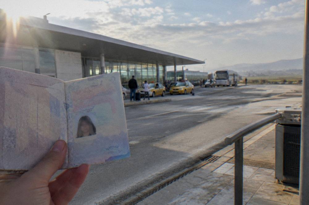 A hand holding a passport open at the photo page in bright daylight