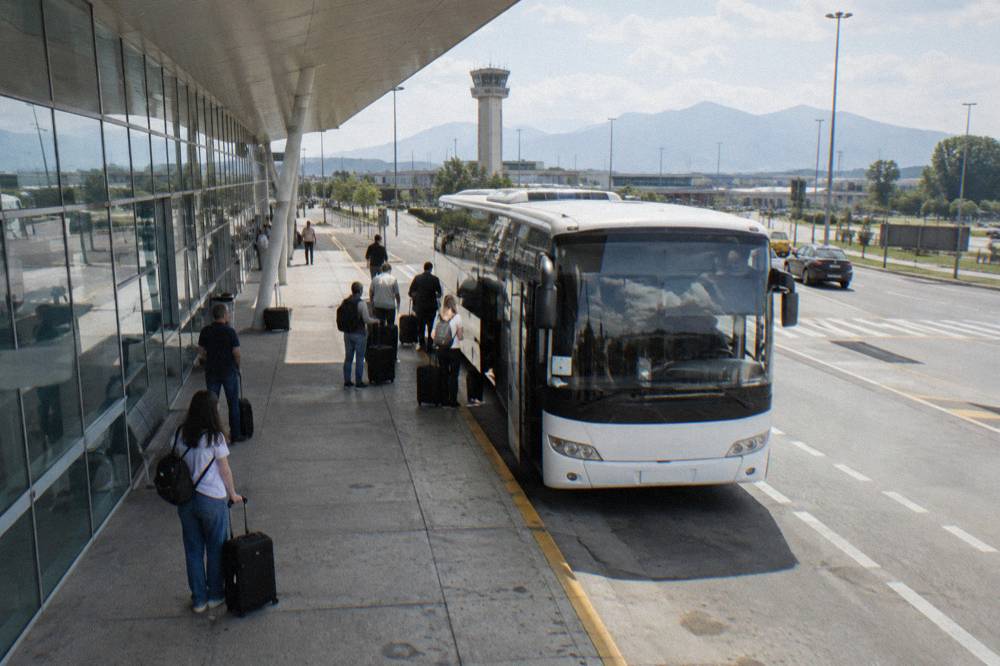 Passengers with luggage waiting beside an airport shuttle bus outside Tirana airport terminal