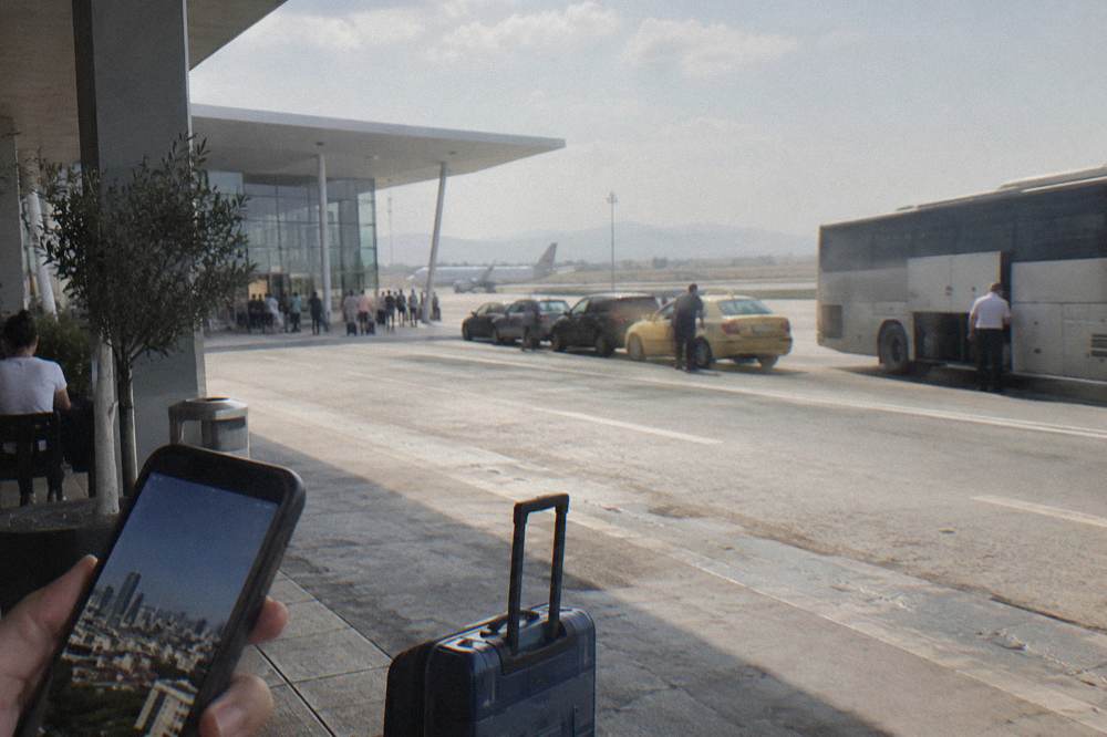 A phone showing a city map app held up above a sunlit square with distant mountains
