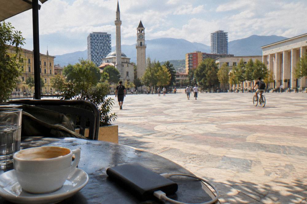 A power bank and charging cable on a cafe table beside a coffee cup in Tirana