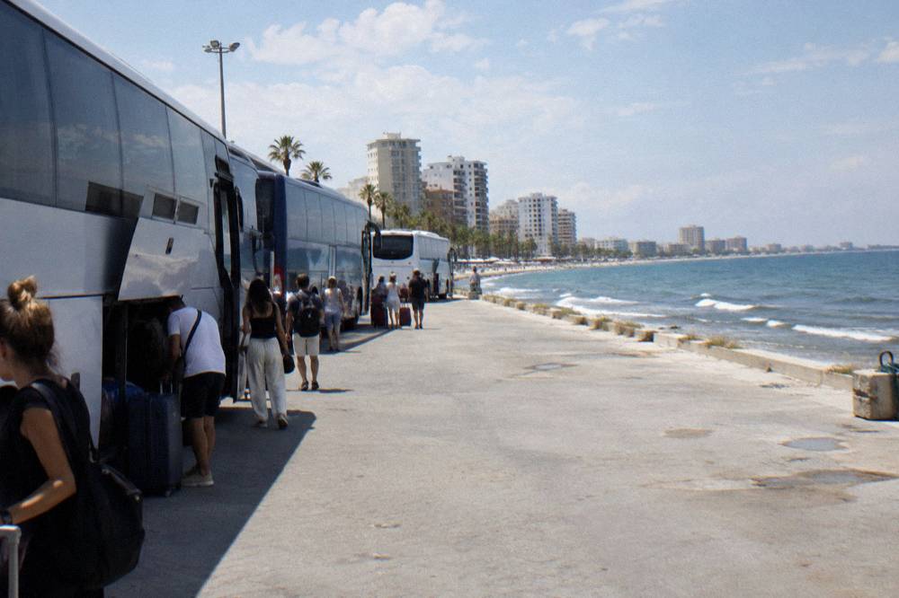 A line of intercity buses parked at a terminal with passengers boarding in daylight