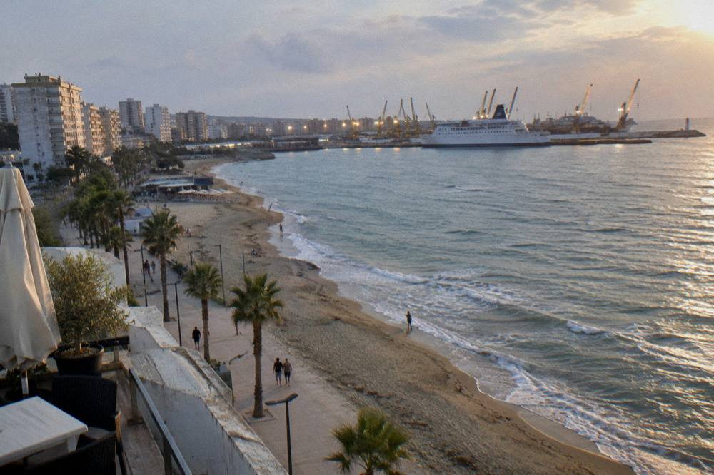 A ferry docked at dusk with the illuminated cranes of Durres port behind it