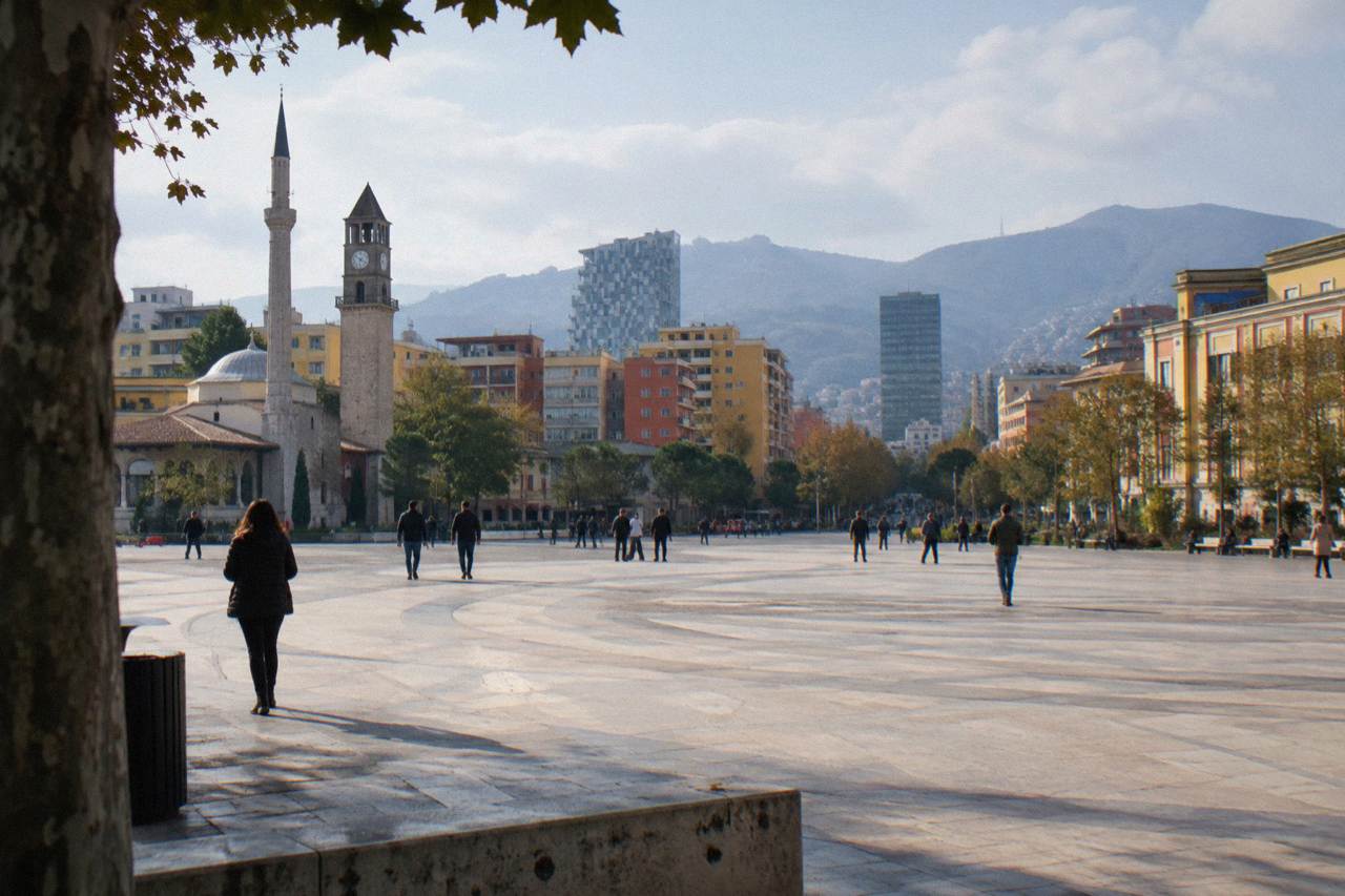Colourful buildings and a boulevard in central Tirana with hills rising behind the city