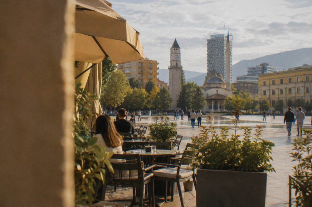 A sunny street in Tirana with cafe tables outside pastel-coloured buildings