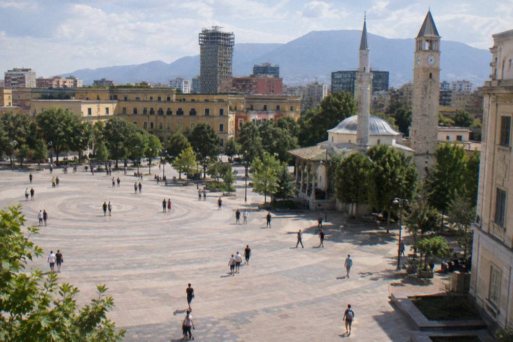 An evening boulevard in Tirana lit by street lamps with people walking