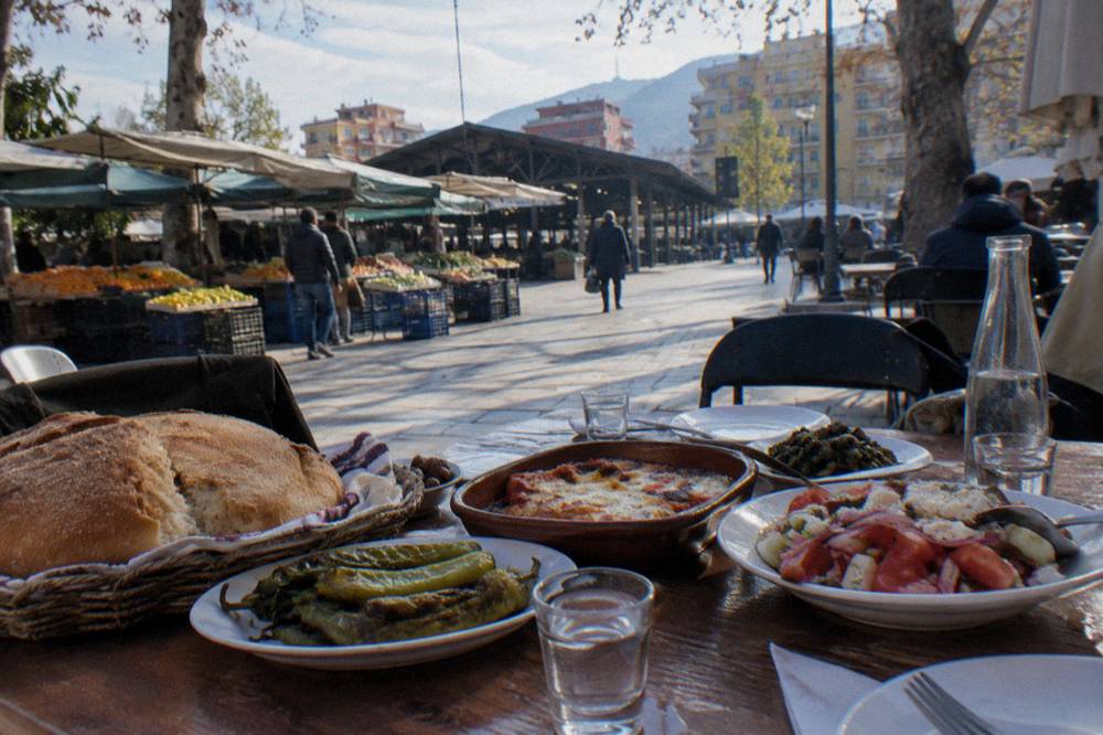 A table filled with shared Albanian dishes, bread and small glasses of raki