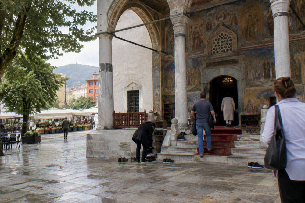 Visitors removing shoes at the entrance of a mosque with a frescoed porch