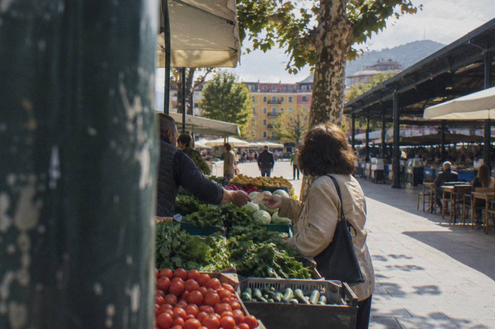 A market vendor handing change in banknotes to a customer at a vegetable stall