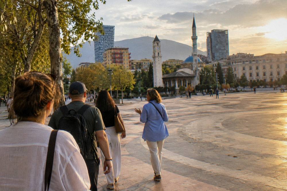 A small group of visitors following a local guide along a tree-lined boulevard in Tirana