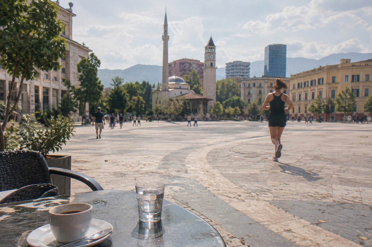A small glass of clear raki on a cafe table beside a coffee cup in Tirana