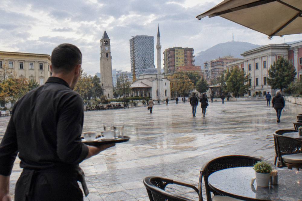 A waiter carrying a tray of coffees to a table on a Tirana street terrace