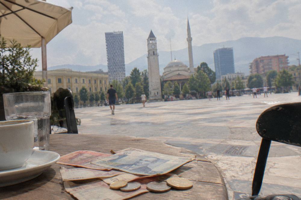 Albanian lek banknotes and coins laid out on a wooden cafe table