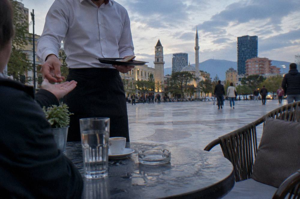 Waiter returning change to a customer at an outdoor cafe table in Tirana