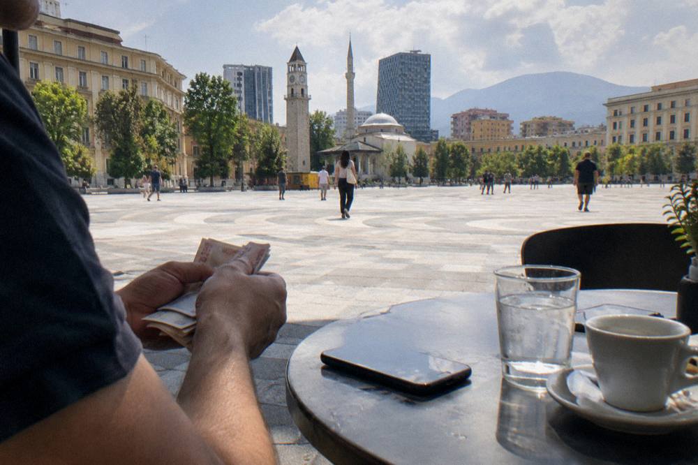 Traveller counting lek notes beside a phone on a cafe table in Tirana