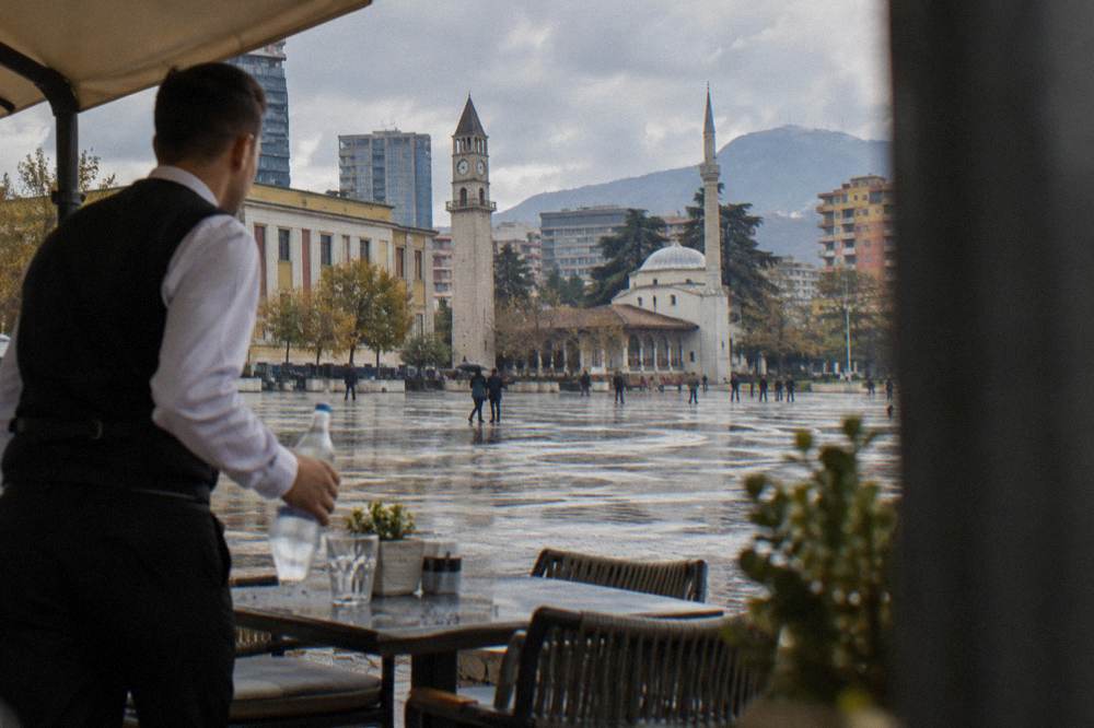 A waiter bringing a bottle of water to a table on a Tirana restaurant terrace