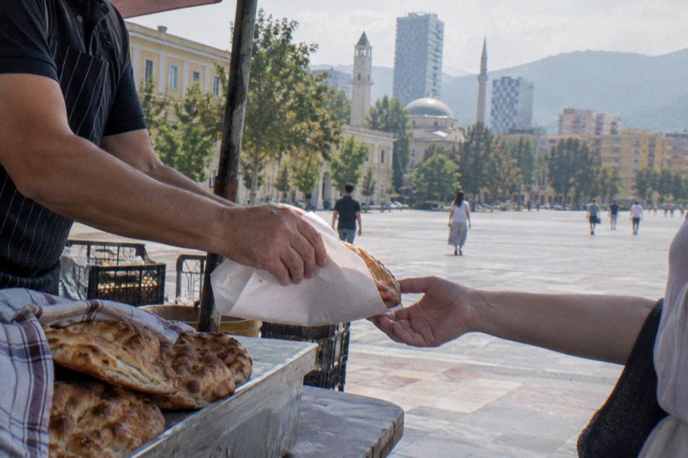 A close view of a market stallholder's hands wrapping bread for a customer in Tirana