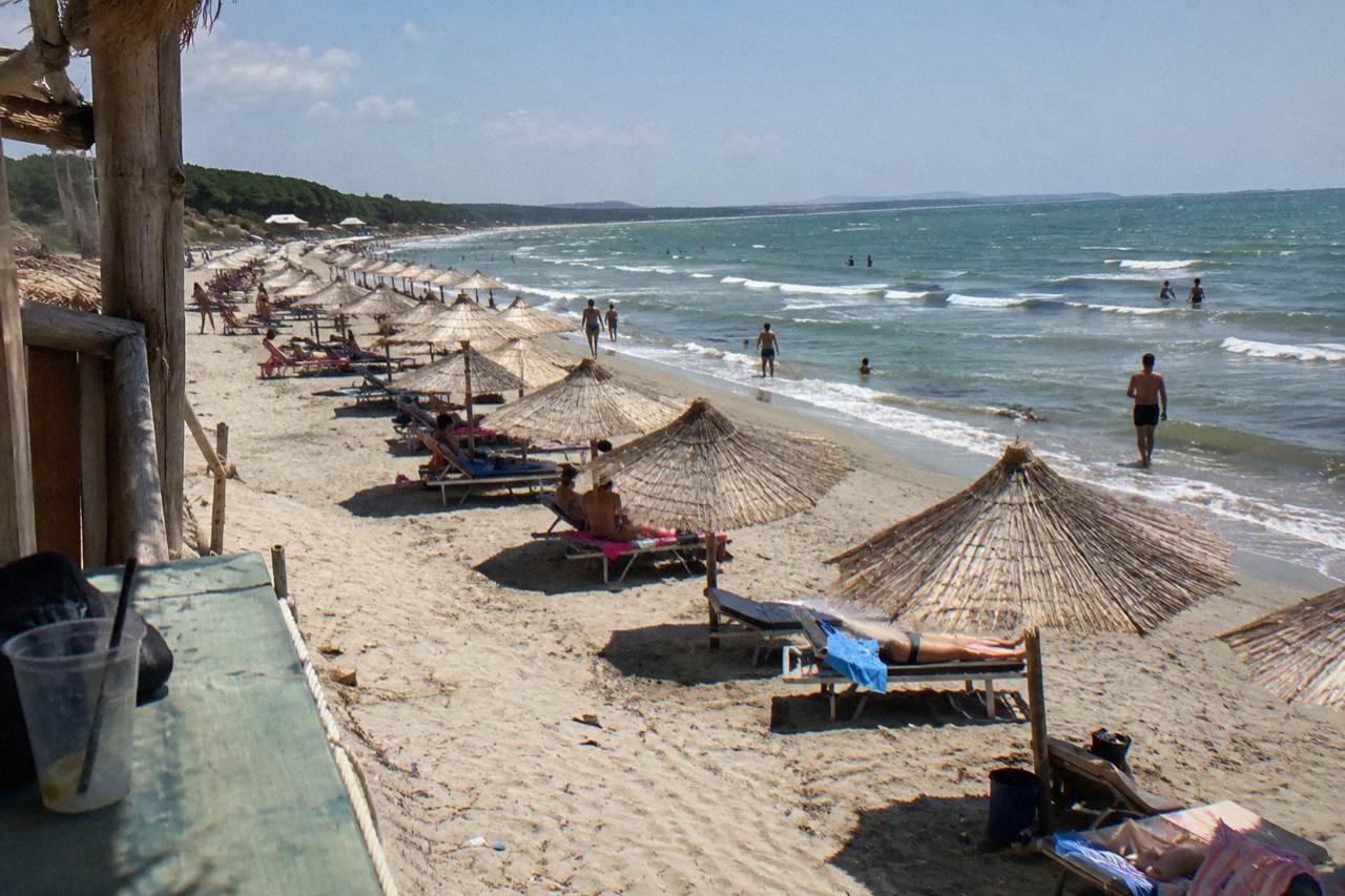 A wide sandy Adriatic beach with sun umbrellas in rows and a calm sea under a clear sky