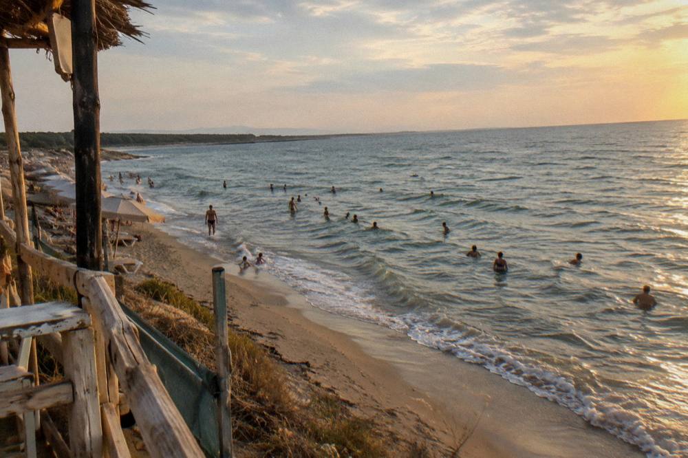 People swimming near a sandy shoreline in late afternoon light