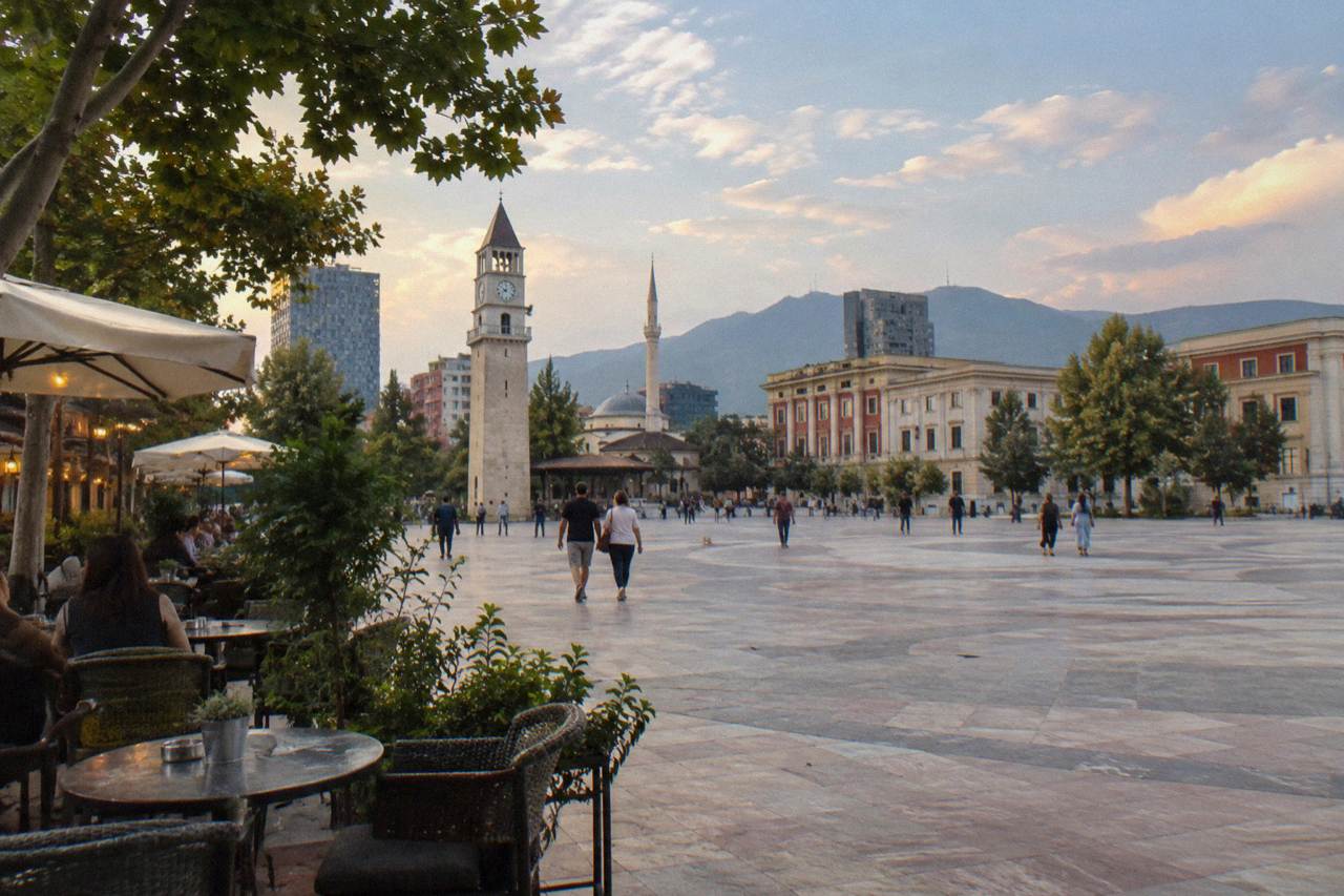 Outdoor cafe tables on a leafy Tirana street in the evening