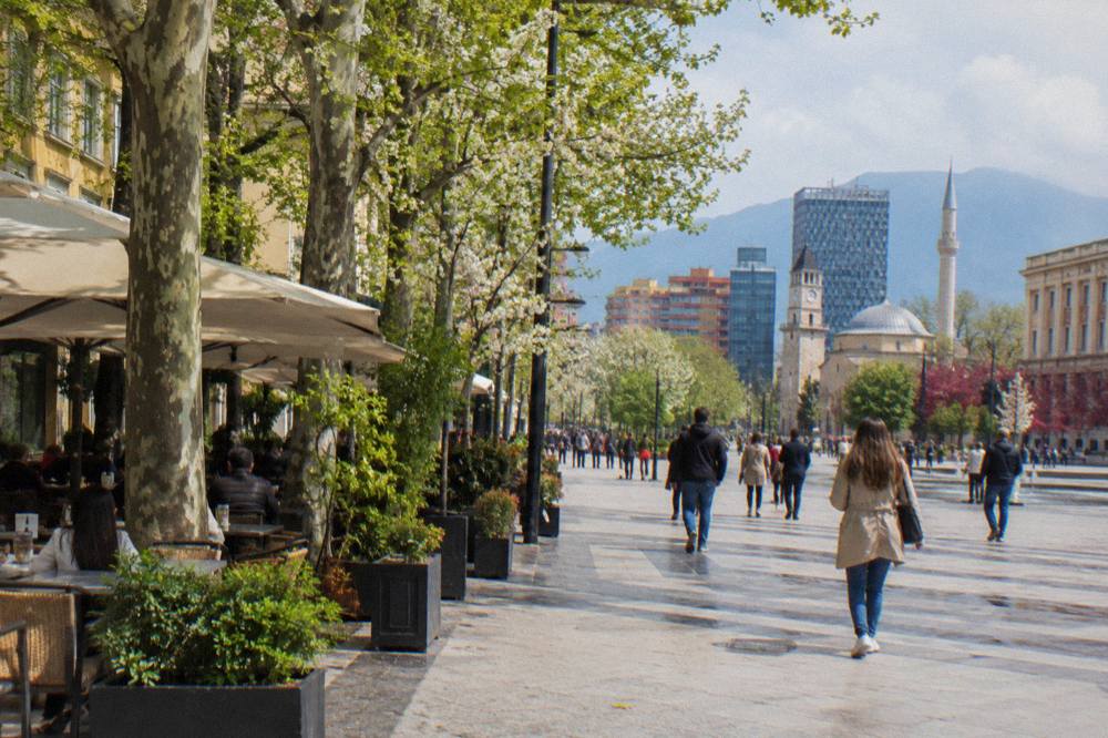 A tree-lined boulevard in Tirana in spring with cafe tables along the pavement