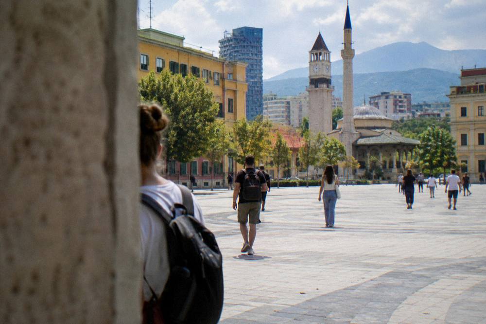 Visitors with daypacks walking past colourful buildings on a Tirana street
