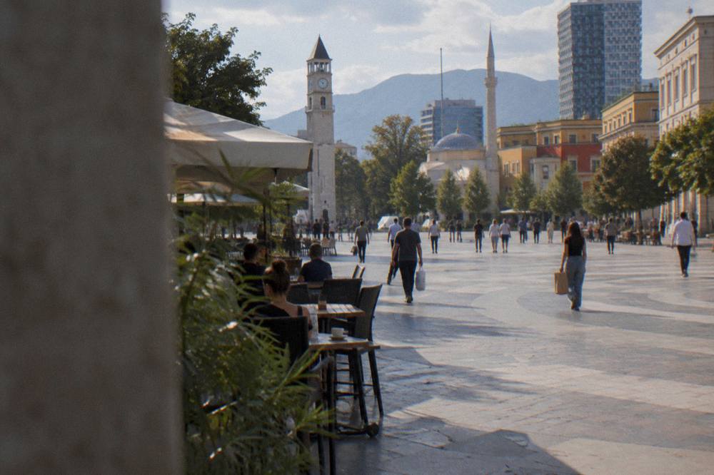 A walking street in central Tirana with cafe tables and people carrying food parcels
