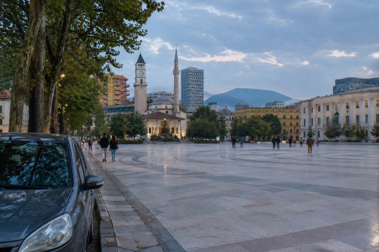 A rental car parked on a tree-lined street in central Tirana with colourful buildings behind it