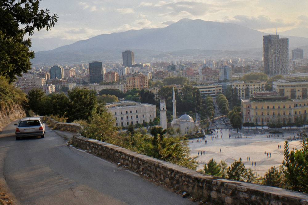 A small hire car on a winding mountain road above Tirana with the city basin below