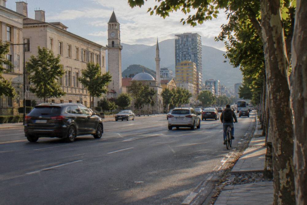 Traffic moving along a wide boulevard in central Tirana in late afternoon light