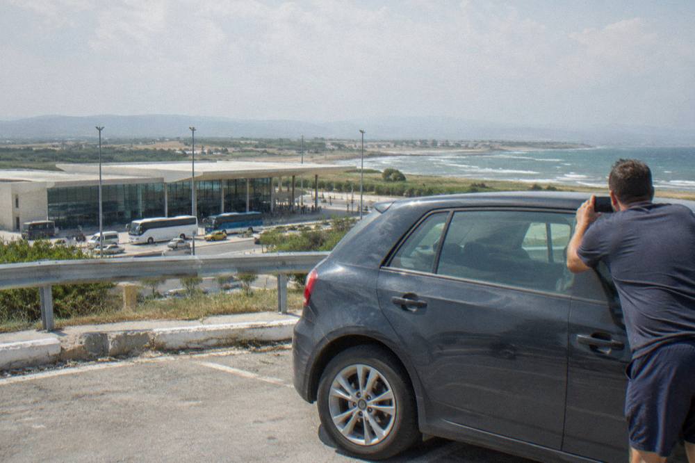 A driver photographing the side panel of a hire car in a car park before departure