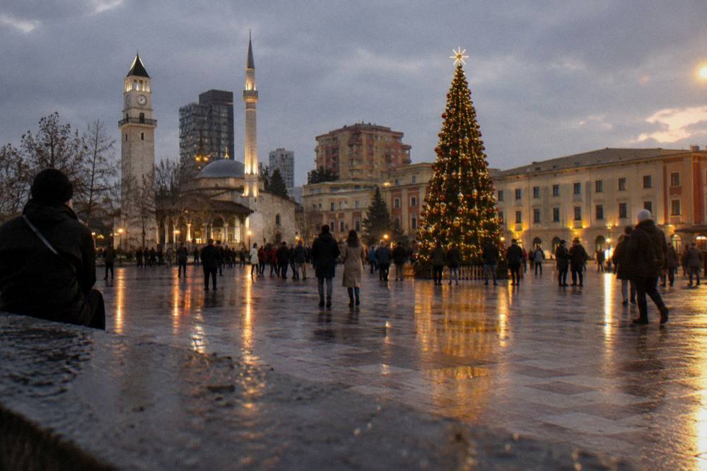 A decorated city square at night with a lit tree and crowds in Tirana