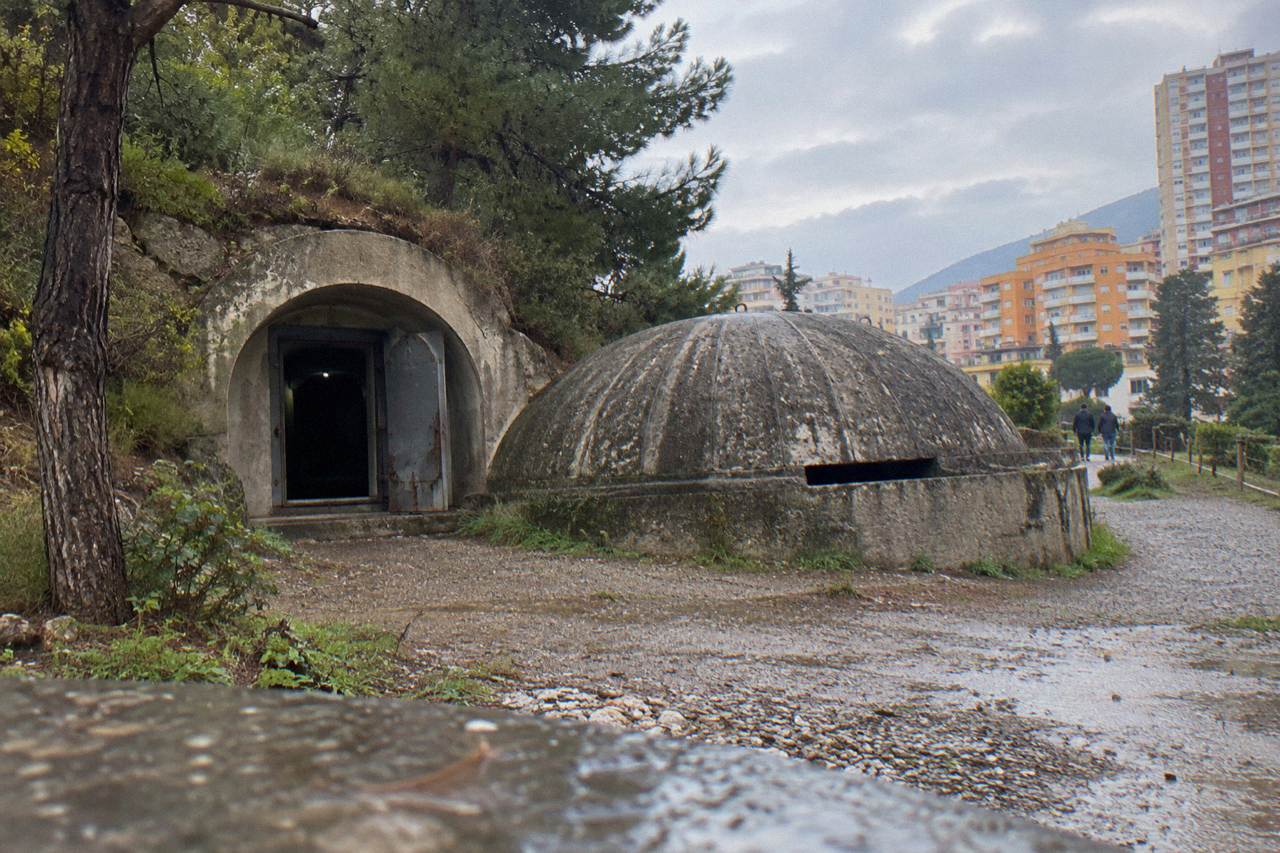 Concrete bunker dome beside a path on the edge of Tirana with apartment blocks behind