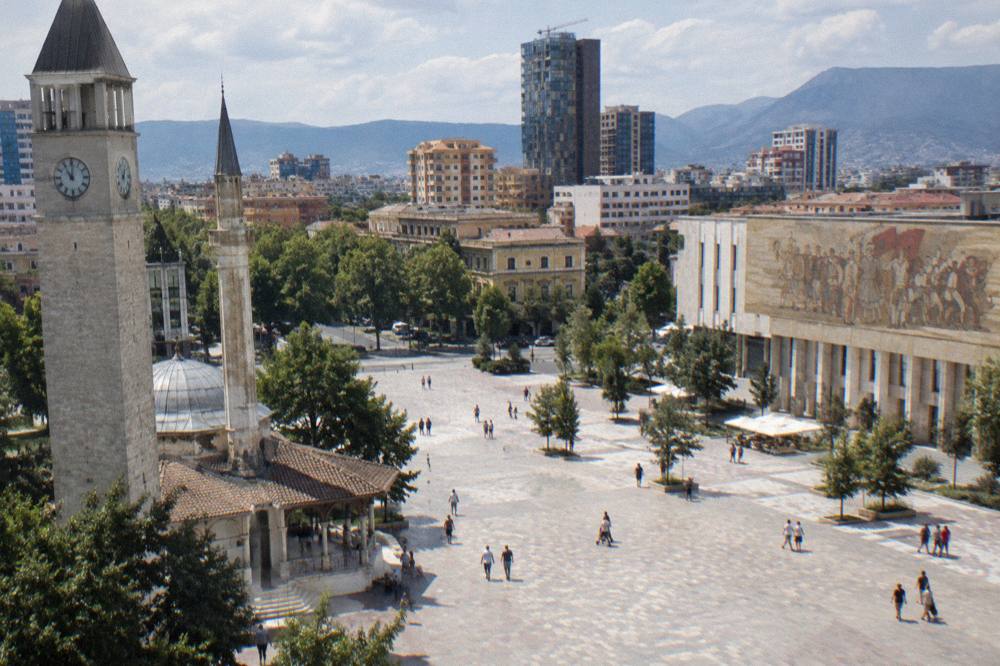 Wide pedestrian square with a mosque, clock tower and large mosaic museum facade