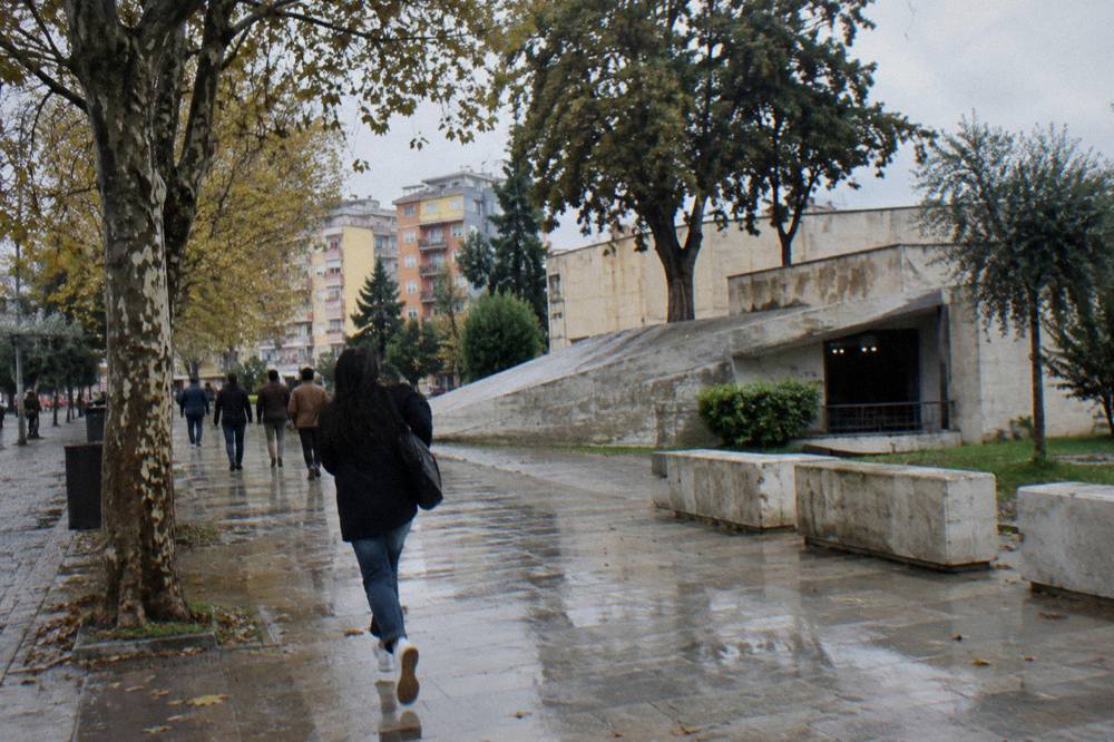 People walking along a tree-lined boulevard past a concrete memorial installation