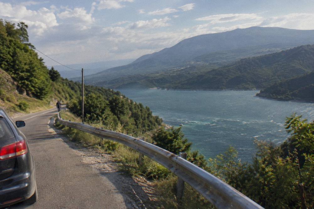 A narrow mountain road winding between green hills above a lake in Albania