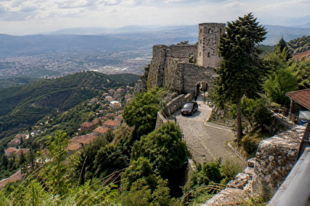 A stone castle on a hillside above a small town with a car parked at its entrance