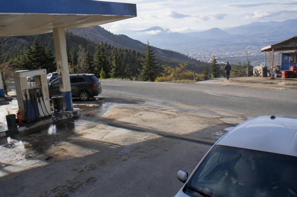 A petrol station forecourt beside a rural road with mountains behind it