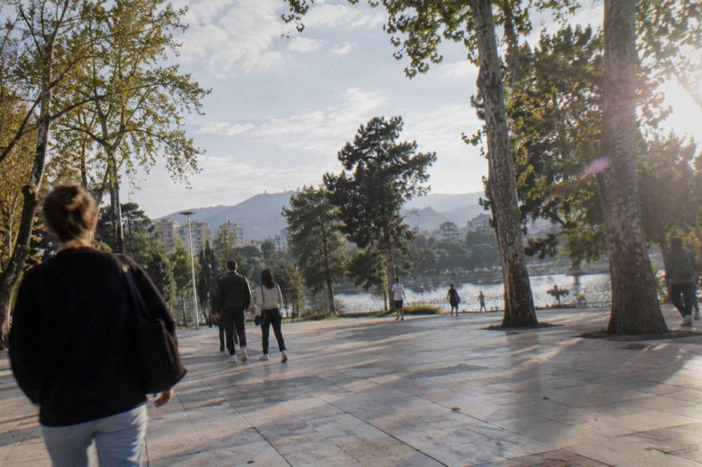 People strolling across a large tiled pedestrian square on a sunny afternoon in a Balkan city