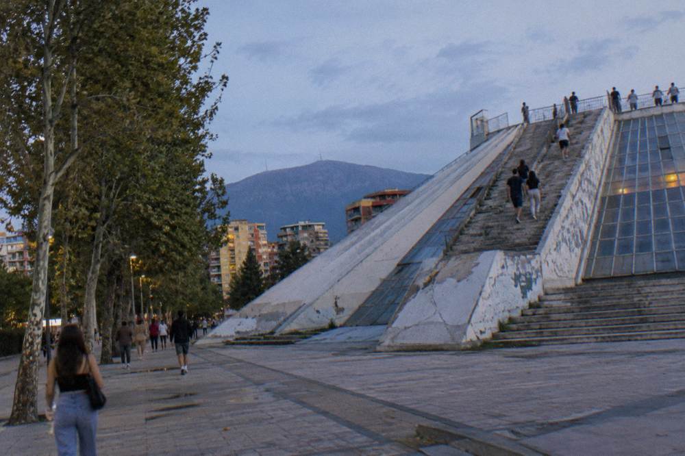 A stepped concrete pyramid structure with people climbing its angled stairs toward a platform