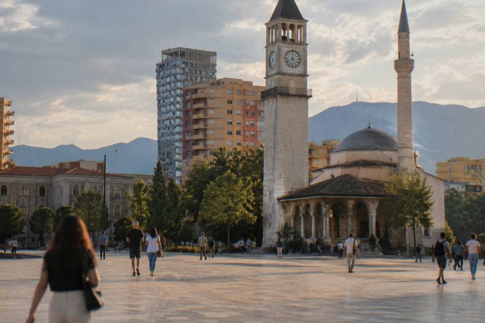Pedestrians crossing the wide open paving of Skanderbeg Square in front of the mosque and clock tower