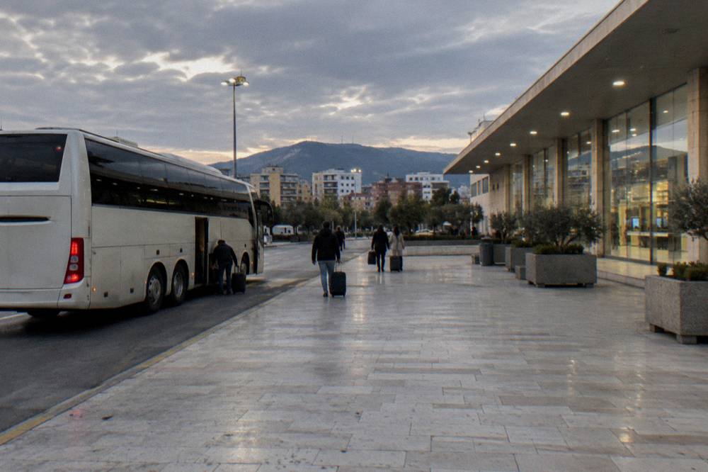 An airport shuttle bus parked at a kerb outside a terminal building at dusk