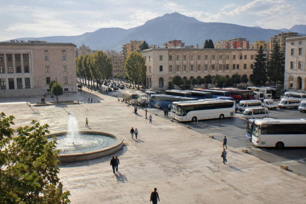 Rows of minibuses and coaches parked in an open-air bus terminal with mountains behind